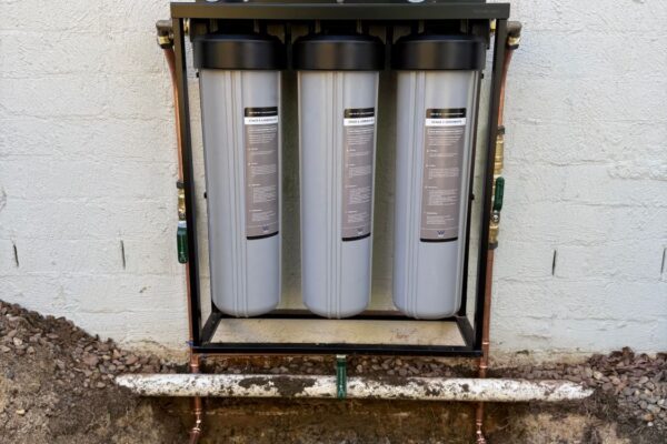 Three stage whole house water filtration system with sediment and carbon filters installed on copper pipework