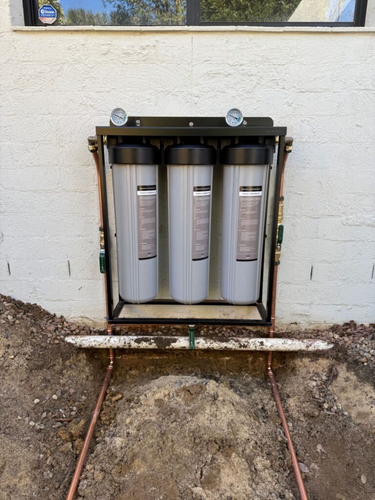 Three stage whole house water filtration system with sediment and carbon filters installed on copper pipework